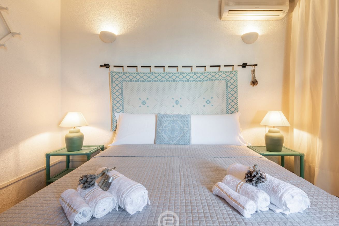 Quarto de hotel com uma cama, duas mesas de cabeceira, duas luminárias e uma cabeceira com padrão decorativo.