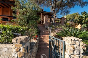 A stone pathway leading to a building with a wooden roof and a metal gate. - Casa Belvedere: Paradise in Costa Rei (Muravera)