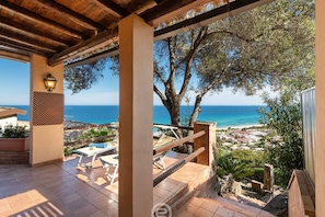 A covered outdoor area with a view of the sea, outdoor furniture, and a pergola structure.
