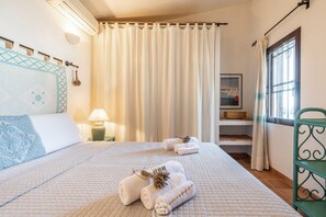 A bedroom with a bed, a nightstand, a lamp, a window with curtains, and a view of the outside.