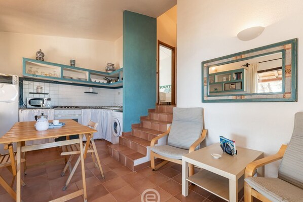 A compact kitchen with a microwave, stove, and washing machine; a dining area with a table and chairs; and a staircase leading to a bedroom.