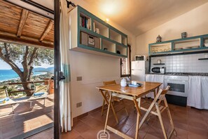 A kitchen with a dining table, chairs, a view of the sea, and a wooden ceiling. - Casa Belvedere: Paradise in Costa Rei (Muravera)