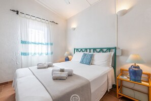 A hotel room with a bed, two bedside tables with lamps, a window with curtains, and a wall-mounted light. - Casa Belvedere: Paradise in Costa Rei (Muravera)