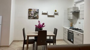 A compact kitchen with a dining table, chairs, a vase with flowers, and a stove.