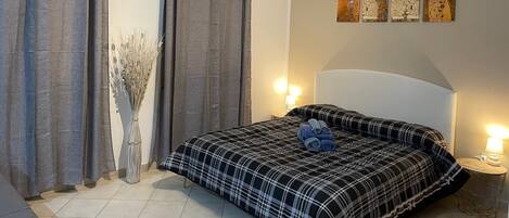 A bedroom with a bed, curtains, a vase with dried plants, and wall art.