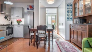 Une cuisine moderne avec des meubles blancs, un réfrigérateur en acier inoxydable et un coin repas comprenant des chaises et une table en bois.