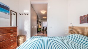 Une chambre avec une couvre-lit à rayures, une commode en bois et une vue sur le salon.