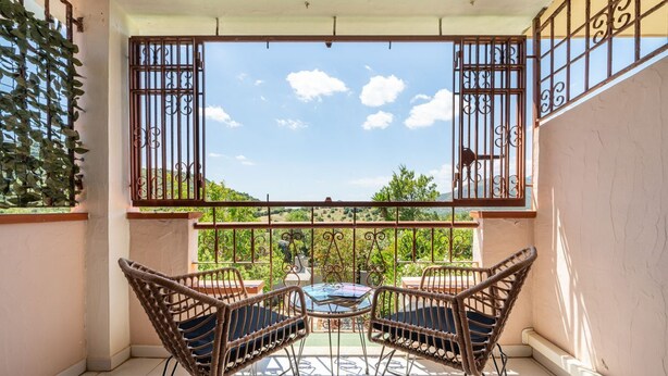 A balcony with a view of a garden, two wicker chairs, and a small table. - Grace's House: Your Oasis of Peace in Villasimius (Villasimius)