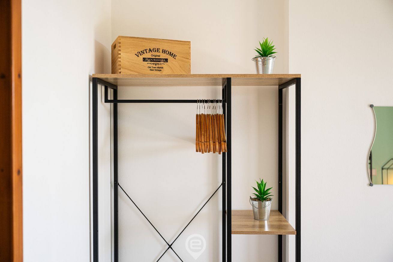 Une étagère en bois ornée d’un panneau décoratif au style rétro, de deux plantes en pot et d’une décoration en bambou suspendue.