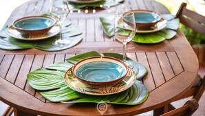 A round wooden table set with green leaf placemats, blue and brown bowls, and wine glasses. - Grace's House: Your Oasis of Peace in Villasimius (Villasimius)