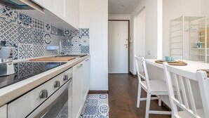 A modern kitchen with patterned tiles, white cabinetry, and a dining area with white chairs and a table.