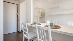 A dining area with a white table, two white chairs, and a white cabinet with shelves.