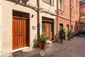 A building with two wooden doors, a tiled ground, and potted plants.