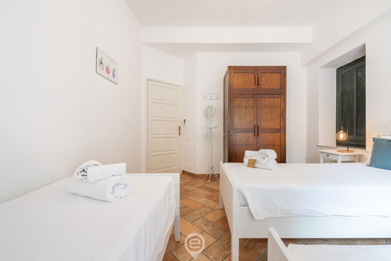 A hotel room with two beds, a wardrobe, a small table, and a lamp.