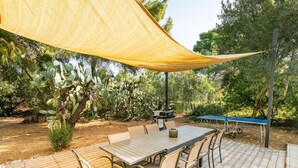 An outdoor patio with a table and chairs, surrounded by greenery and a yellow shade sail. - Casa Flamingo - Next to the sea (Santa Margherita di Pula)