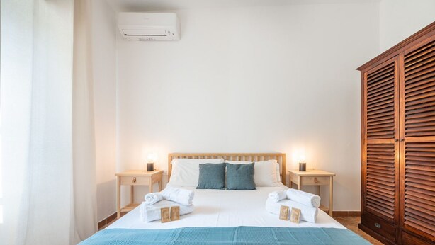 A neatly made bed with white and blue linens, two bedside tables with lamps, and a wooden wardrobe. - Casa Flamingo - Next to the sea (Santa Margherita di Pula)