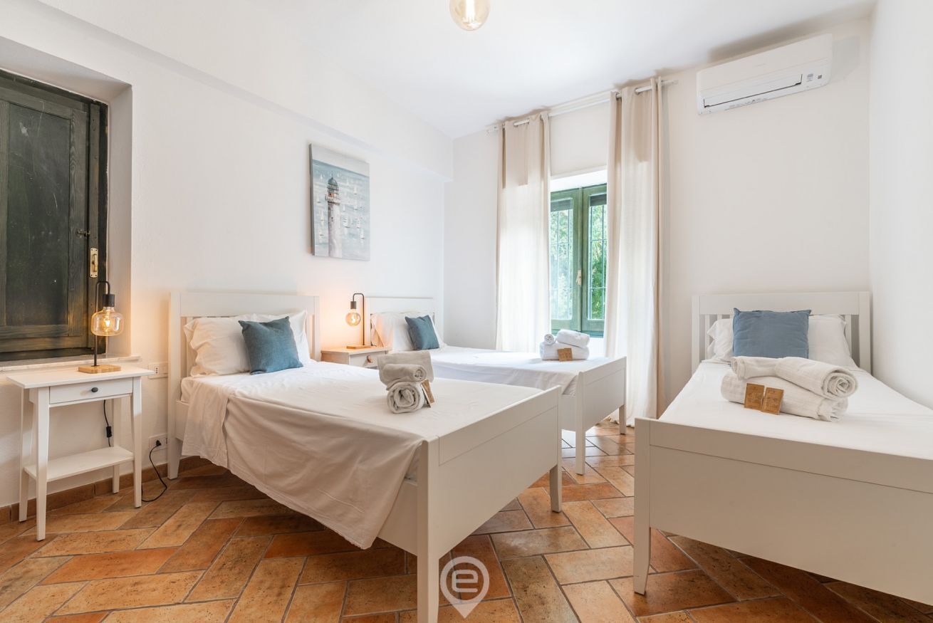 A hotel room with two beds, a desk, a chair, a lamp, and an air conditioning unit.