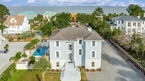 A multi-story building with a swimming pool, surrounded by lush greenery and a view of the sea. - Luxury Beach House, Private Pool & Jacuzzi, Ocean Views by Tybee Cottages (Tybee Island)