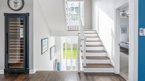 A staircase leading to a second floor, a door with a frosted glass panel, and a clock with a pineapple design on the wall. - Luxury Beach House, Private Pool & Jacuzzi, Ocean Views by Tybee Cottages (Tybee Island)