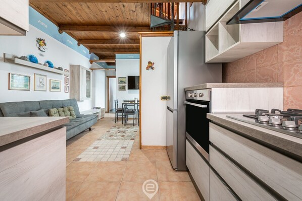 Eine moderne Küche mit Einbauofen, eine Essecke mit Tisch und Stühlen sowie ein Wohnbereich mit Sofa und Wanddekoration.