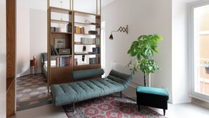 En moderne stue med sofa, bogreol, radiator og en stor plante.