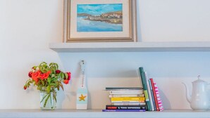 Uno scaffale con un quadro incorniciato, un vaso di fiori, un termometro, una pila di libri e un bollitore.