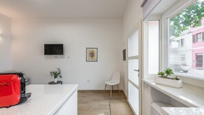 A modern kitchen with a red toaster, a flat-screen TV, a framed picture, and a window with a view of buildings.
