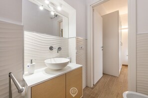 Een moderne badkamer met een witte wastafel, een grote spiegel en een houten wastafelmeubel.