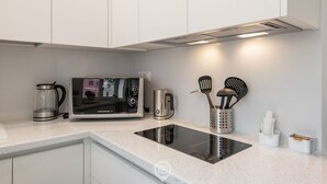 A modern kitchen with white cabinetry, a built-in microwave, a coffee maker, and an induction cooktop.
