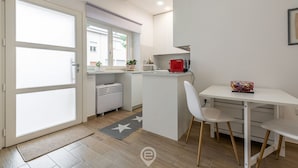 A compact kitchen with a small island, a white dining table with two chairs, and a red kettle on the counter.