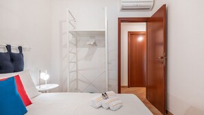 Una camera d'albergo con un letto, un comodino con una lampada, un armadio e un condizionatore.