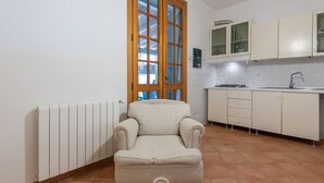 Una stanza piccola e arredata, con termosifone, una finestra con stipiti in legno e un angolo cottura con mobili e lavello.