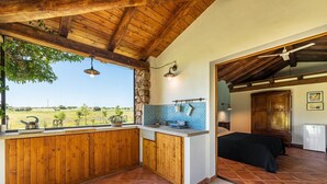 A rustic kitchen with wooden cabinets, a stone wall, and a view of the countryside.