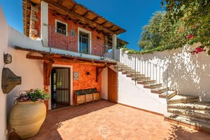 Ein zweistöckiges Gebäude mit einem hölzernen Balkon, einem großen Topf mit Pflanze und einer Treppe, die zum oberen Stockwerk führt.