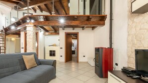 A living room with a grey sofa, a red and black entertainment unit, and a stone wall. - Maty's House (Gonnesa)