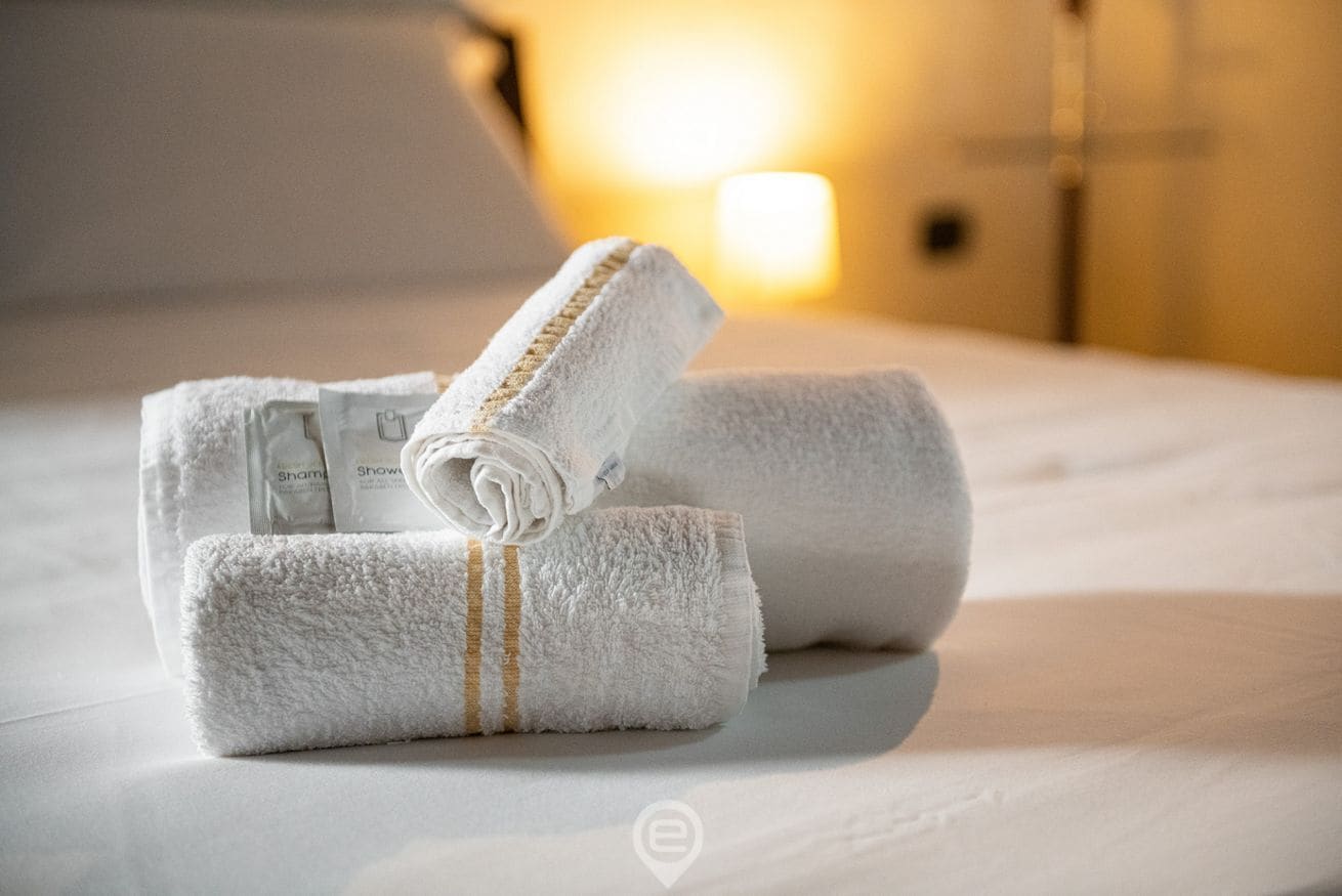Neatly folded white towels with a gold stripe on a bed in a hotel room.