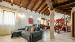 A spacious living room with a large L-shaped sofa, a stone pillar, and a staircase leading to an upper level. - Maty's House (Gonnesa)