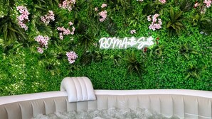 A hot tub with a white cushion and a sign that reads "ROMANTIC Suite" against a backdrop of green foliage and pink flowers. - Colosseum ★★★★★ - Rooftop with HOT jacuzzi and Skyline of Rome (Roma)