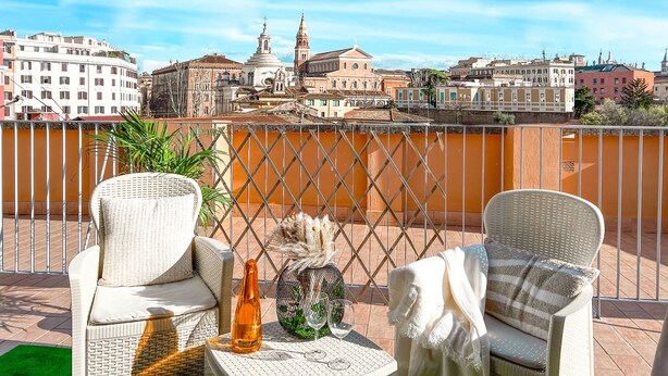 A balcony with wicker chairs, a table with a bottle and glasses, and a view of historic buildings. - Colosseum ★★★★★ - Rooftop with HOT jacuzzi and Skyline of Rome (Roma)