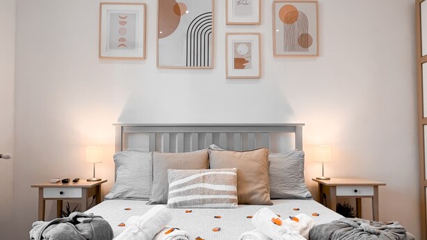 Una cama bien hecha con toallas enrolladas y pétalos de rosa, mesitas de noche con lámparas y cuadros en la pared.