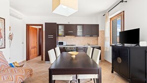 A modern kitchen with dark cabinets, a dining table with chairs, a TV on a cabinet, and a window with curtains. - Antonella's Apartment (Alghero)