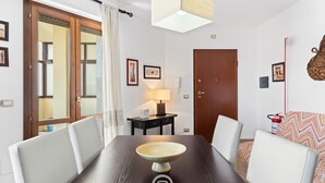 A dining area with a wooden table, white chairs, a bowl centerpiece, a lamp, and a door with a mirror. - Antonella's Apartment (Alghero)