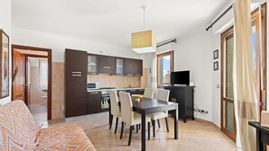 A modern kitchen with dark cabinets, a dining table with chairs, a TV, and a sofa in a living area. - Antonella's Apartment (Alghero)