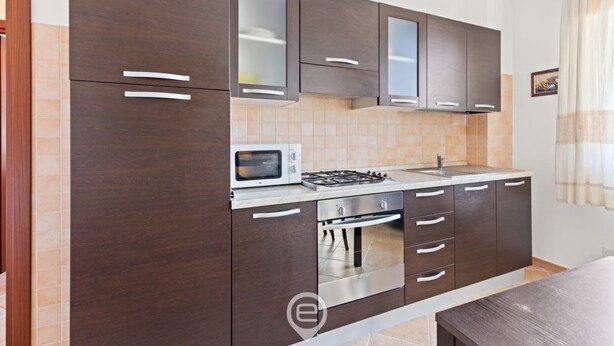 A modern kitchen with dark wooden cabinets, a built-in microwave, a gas stove, and a stainless steel oven. - Antonella's Apartment (Alghero)