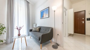 Ein modernes Wohnzimmer mit einem grauen Sofa, einem kleinen runden Tisch mit einer Vase, einer Stehlampe und einer Tür zu einem weiteren Raum.