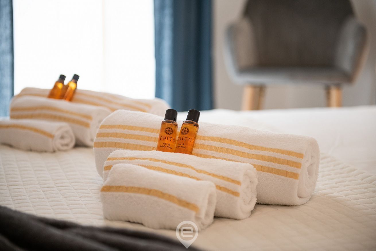 A neatly made bed with rolled white towels and two bottles of hair and body wash.