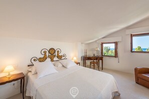 A bedroom with a bed, a desk, and a view of the sea.