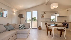 Una sala de estar moderna con un sofá, una mesa de comedor con sillas, una lámpara y una zona de cocina con armarios y un refrigerador.