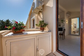 A balcony with potted plants and a sliding door, leading to an interior room with a chair and a television.