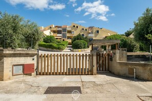 A gated residential area with a multi-story building, a covered entrance, and a small garden.